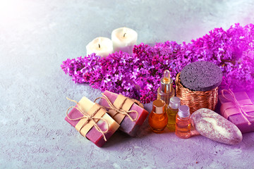 Fototapeta na wymiar SPA still life with handmade soap, aroma candles, lilac flowers, aromatic oils and stones on the stone background.