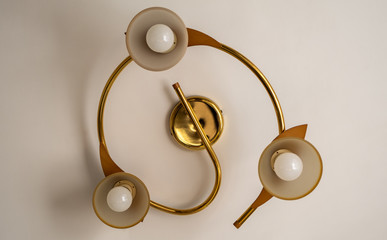 Gold chandelier with three lamps mounted on the ceiling of the apartment.