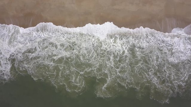 Flying over a sandy beach. Waves break on a sandy beach on the Atlantic coast, aerial View. Nazare, Portugal. (raw video).
