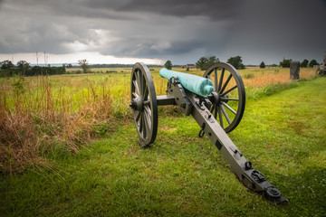 A civil war cannon points across the battlefield at Cemetery Ridge as storm clouds gather