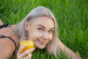 Sexy blonde woman with orange juice on a background of green grass close-up