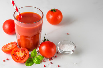 Tomato juice in a glass with a straw, fresh tomatoes, salt, basil and pepper