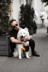 Portrait of a young man with a  Cute  beautiful  Samoyed dog in a park  with owner outdoors