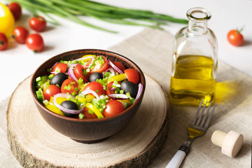 Vegetable salad with fresh tomatoes, cucumbers, paprica, onions and canned olives in a brown bowl. Glass bottle with olive oil. Healthy food. Vegetarian food.