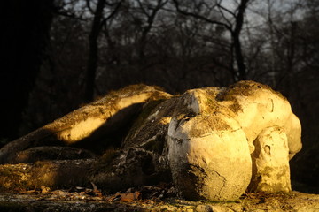 Fototapeta na wymiar Decaying mossy sculpture in a garden dramatically lit by golden hour. Figure man lying on his back 
