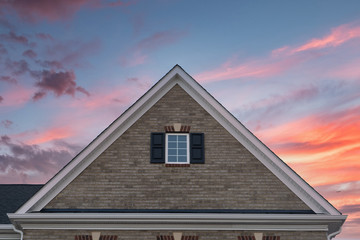 Gable roof covered with light colored brick framed by a fascia, attic window with decorative trim...