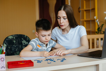 Fototapeta premium A mother and her child are engaged in distance learning at home in front of the computer. Stay at home, training