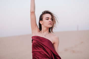 Fototapeta na wymiar portrait of a young slender girl in a red dress in the wind in the desert