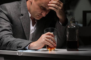 A man with bottle of whiskey on the kitchen. The concept of drunkenness and alcoholism. Alcoholic father. A tired sick man in sorrow drinks alone. Emotional experience. selective focus