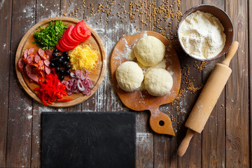 Pizza dough with ingredients on wood table and stone cutting board, shot from above. Top view