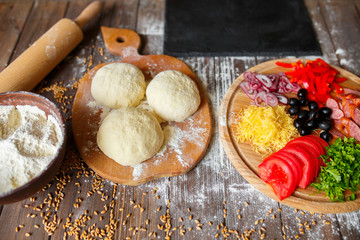 Pizza dough with ingredients on wood table and stone cutting board, shot from above. Top view