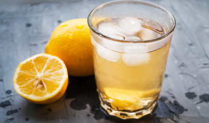 Homemade lemonade with ice in a glass. Glass, lemons and drops on a gray background.