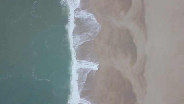 Flying over a sandy beach. Waves break on a sandy beach on the Atlantic coast, aerial View. Nazare, Portugal. (raw video).