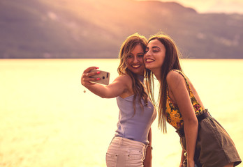  Two smiling young women on beach making selfie with smartphone.