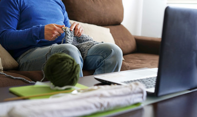 Young man watching lesson online and knitting from home