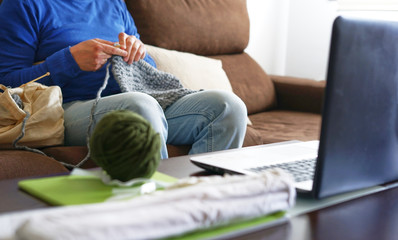 Young man watching lesson online and knitting from home