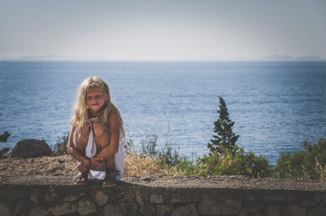 girl with long blond hair sitting by the sea and waiting
