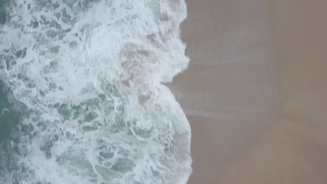 Flying over a sandy beach. Waves break on a sandy beach on the Atlantic coast, aerial View. Nazare, Portugal. (raw video).