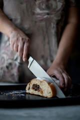 Obraz na płótnie Canvas Female hands cut with a knife. Delicious pastry stuffed with raisins, nuts and chocolate. Lying on a baking sheet sprinkled with powdered sugar