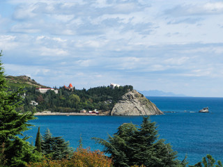 panoramic view of the sea, a rocky cape and coniferous trees in the foreground