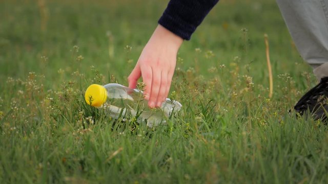 girl's hand raises an empty plastic bottle lying on the grass in the park