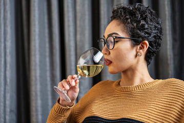 A woman wearing glasses and a sweater drinking white wine