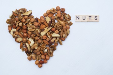 Different nuts in form of heart. Brazil nuts, walnuts and hazelnuts on white wooden background. Healthy food concept. Vegetarian food. 