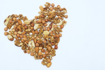 Different nuts in form of heart. Brazil nuts, walnuts and hazelnuts on white wooden background. Healthy food concept. Vegetarian food. Fresh food. Raw food.