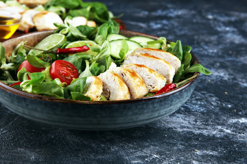Healthy salad bowl with tomatoes, chicken and mixed greens, lettuce. Food and health bowl with cucumber on table