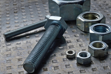 Bolts and hex nuts of various sizes, laid out on a metal surface. assorted closeups.