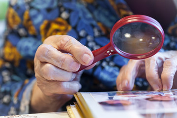 An old grandmother reads a newspaper with a strong magnifying glass with a pen. Color photo....