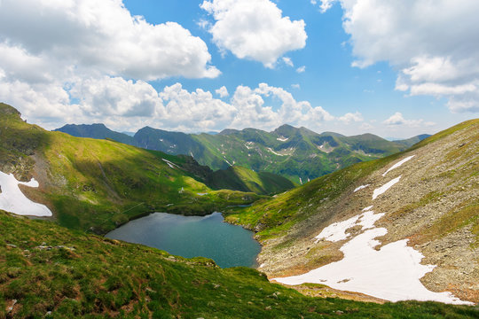 beautiful nature of romania mountains. lake capra in the valley. hills covered in grass, rocks and snow. wonderful summer sunny day with gorgeous cloudscape