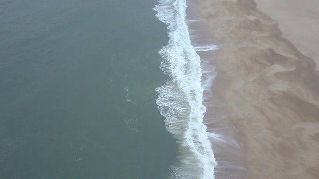 Flying over a sandy beach. Waves break on a sandy beach on the Atlantic coast, aerial View. Nazare, Portugal. (raw video).