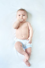 a wonderful baby lies on a white sheet for six months and wants to cry . the hand in his mouth. teething