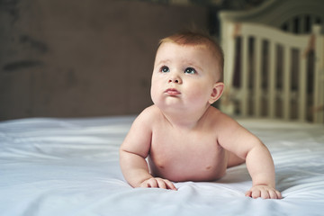 a wonderful six month old baby lies on a large bed on a white sheet and looks up