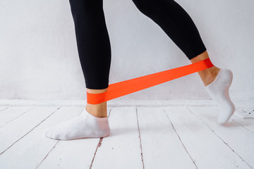 The concept of sports training at home. The girl does exercises for the arms and legs using fitness gum. Strengthens the muscles in the body with a red color rubber band with strong resistance
