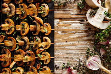 Mushroom skewers with herbs and garlic on a cast iron grill plate and raw skewer ingredients with...
