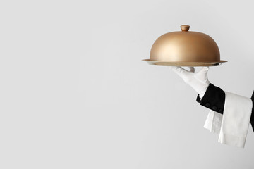Hand of waiter with tray and cloche on grey background