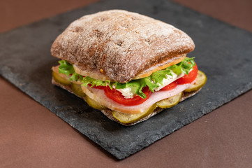 A sandwich on a tray. Sandwich with meat and vegetables on a black granite stand. Special square roll for sandwiches.