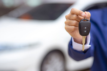 Close up of dealer giving key to new owner and shaking hands in auto show.