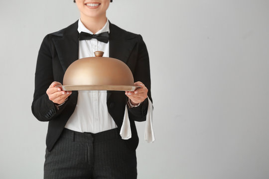 Female waiter with tray and cloche on grey background