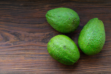 Three avocados on a wooden table.
