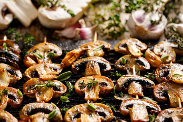 Mushroom skewers with herbs and garlic marinade on a cast iron grill plate  close up 