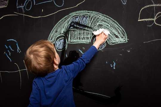 little boy erases the drawing from the board. chalk drawn cars on black background. children's creativity.