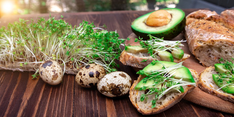 sandwiches with avocado and microgreens, quail eggs on a wooden background. healthy diet. serving option. the process of making breakfast.