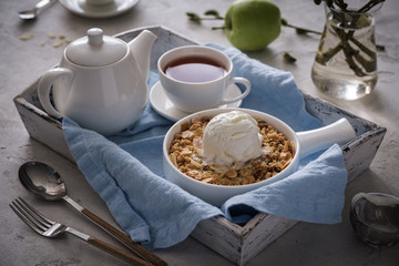 Apple crumble with a scoop of vanilla ice cream and tea on a wooden tray. Breakfast concept
