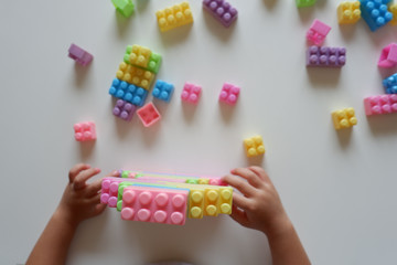 Close up of child's hands playing with colorful plastic bricks at the table. Toddler having fun and building out of bright constructor bricks. Early learning. stripe background. Developing toys