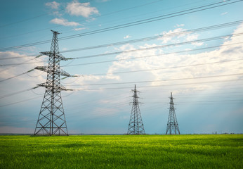 High voltage lines and power pylons in a flat and green agricultural landscape on a sunny day with clouds in the blue sky. Cloudy and rainy. Wheat is growing © es0lex