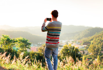 Young man taking photo of landscape with smartphone