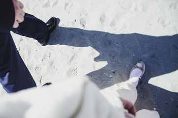 Couple is walking on the beach after marriage ceremony. He is wearing military uniform and she wears light pink dress.  